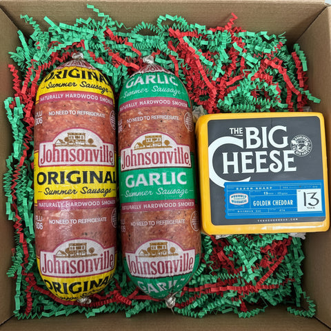 Two Johnsonville summer sausages and a block of cheese in a box with shredded paper.